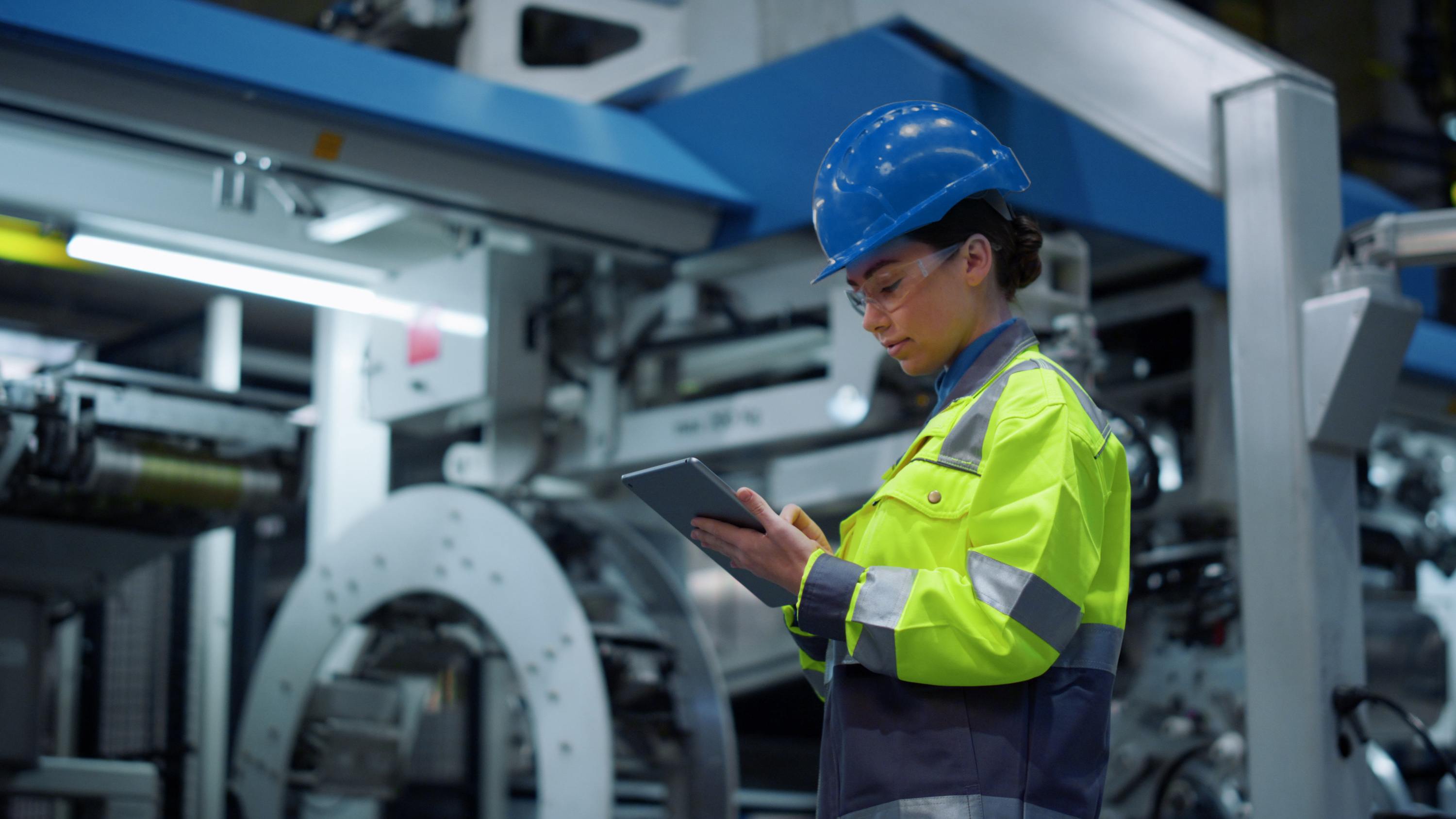 A woman in safety clothing checks process sequences of a machine on a tablet.